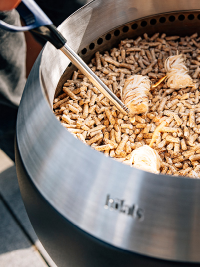 Eine Person zündet Holzspäne in einem Feuerkorb an. Zeigt, wie man den MOON 45 entzündet.