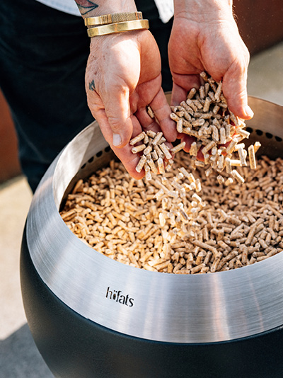 Eine Person gibt Holzspäne in einen Feuerkorb. Zeigt, wie man den MOON 45 anzündet.