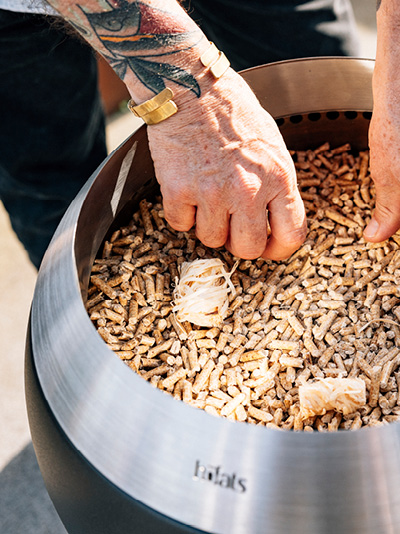 Eine Person legt Holzspäne in einen Feuerkorb. Zeigt, wie man den MOON 45 anzündet.